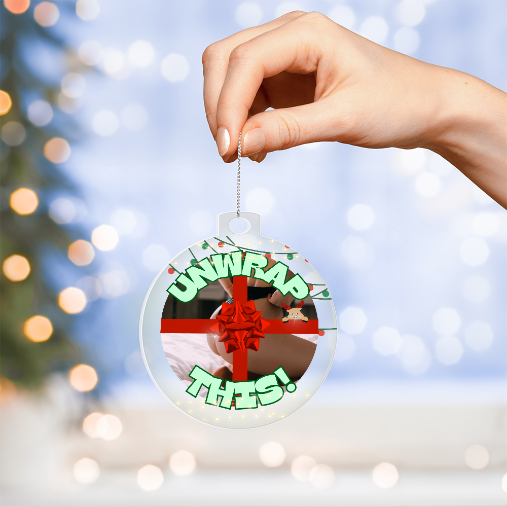 Naughty holiday acrylic ornament with “Unwrap This” design being held by a hand